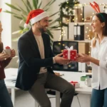 Happy coworkers in a modern office wearing festive hats and exchanging wrapped Secret Santa presents, illustrating fun and thoughtful secret Santa gift ideas for coworkers.